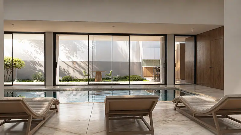 Rendu 3D d'une piscine intérieure de luxe avec transats en bois et sol en marbre dans une villa moderne en Algérie. Ouvert sur un patio.